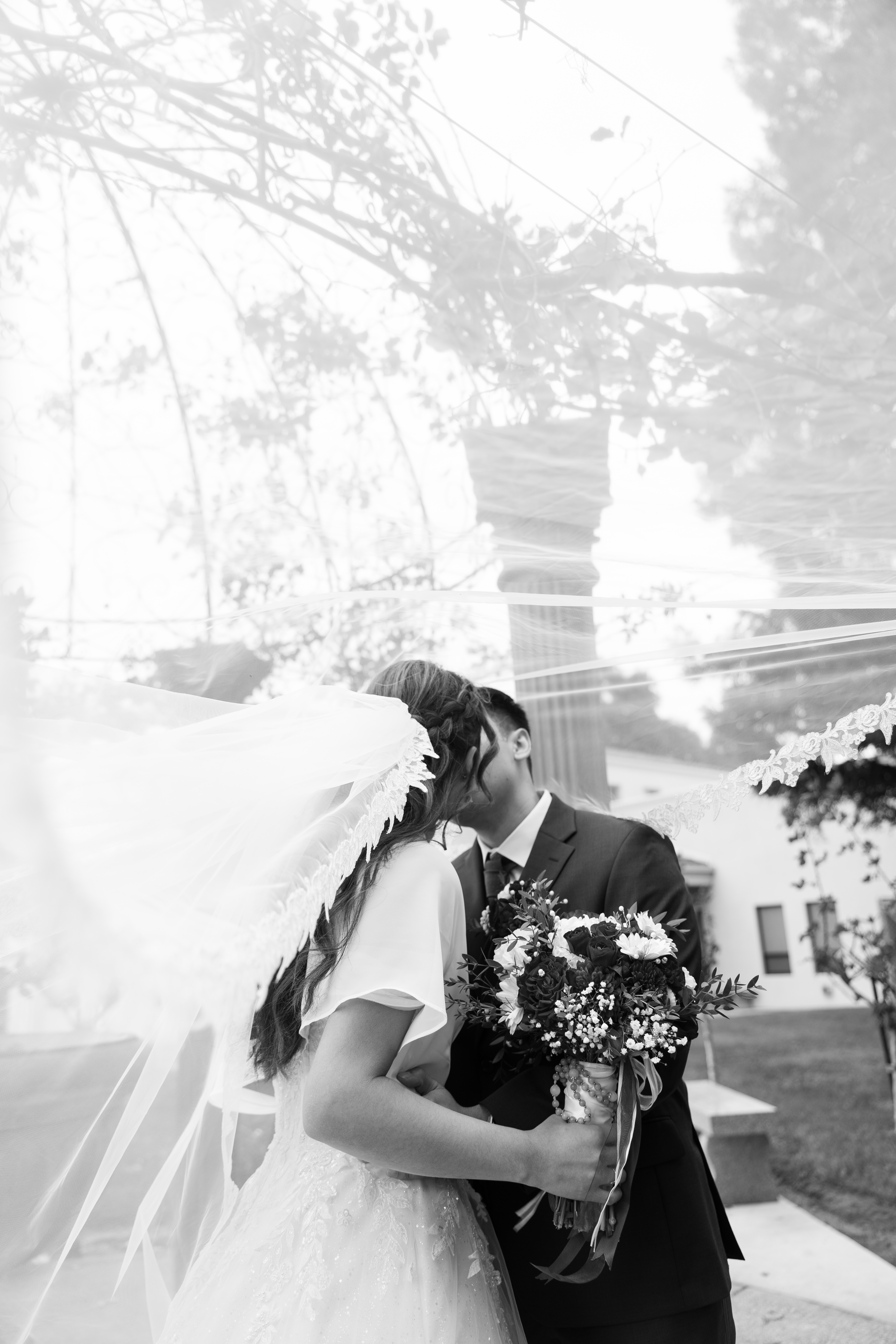 Bride and groom kissing with veil flowing in the wind, black and white